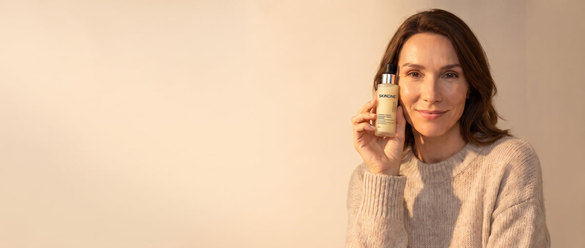 Vrouw in herfsttrui houdt het SKINTONE Vitamine C serum naast haar wang